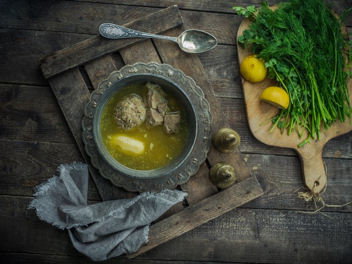 Soup with meatball and meat on wooden surface with dill and lemons