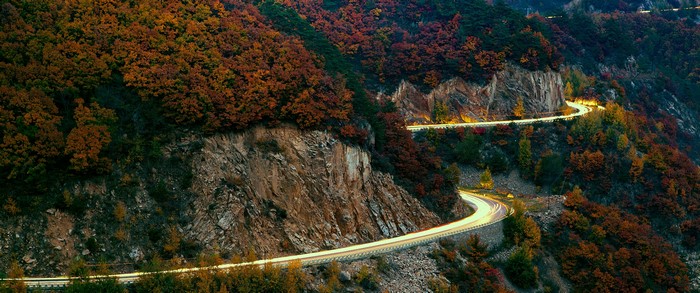 Winding mountain road with autumn foliage and light trails