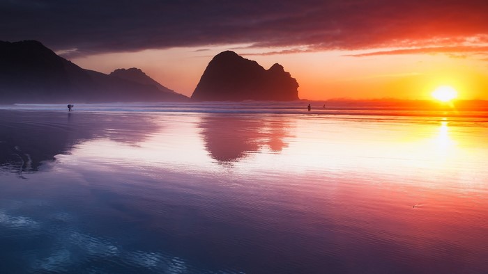 Sunset over a beach with waves and rocks in New Zealand