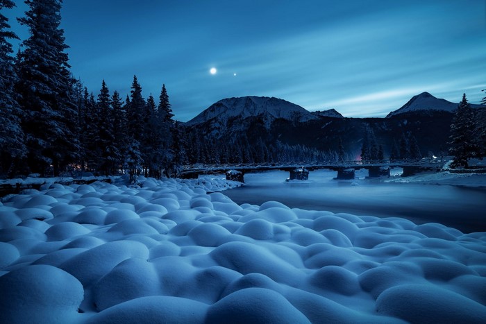 Snowy landscape with mountains and a bridge at night