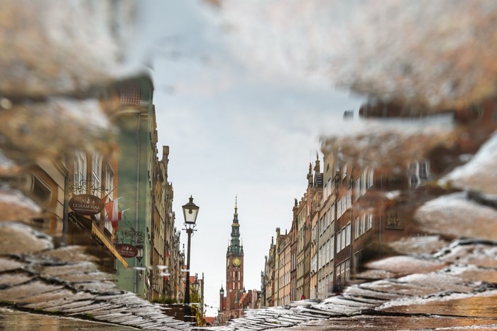 Reflection of Gdańsk street with clock tower in puddle