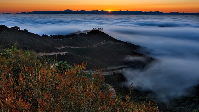Sunset over clouds with mountains and winding road