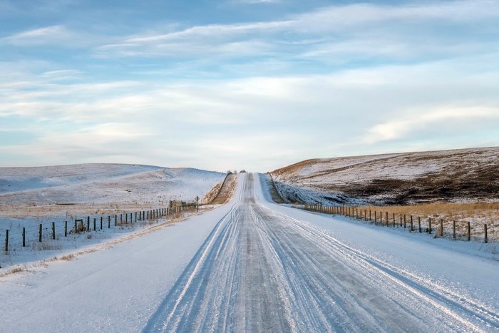 Snowy road through rolling hills under a cloudy sky