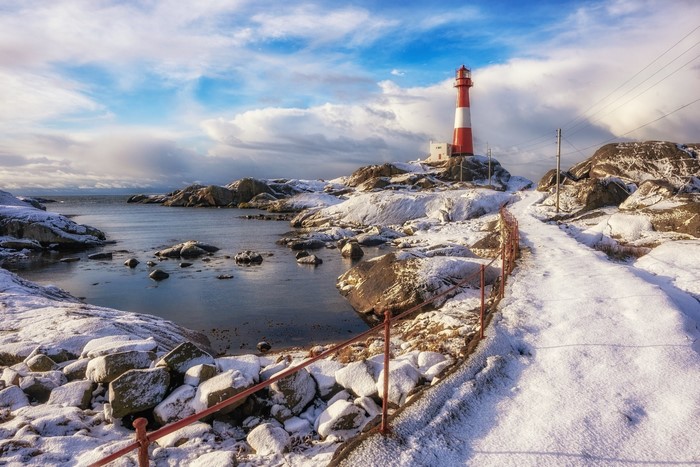 Red and white lighthouse on a snowy coast in Norway