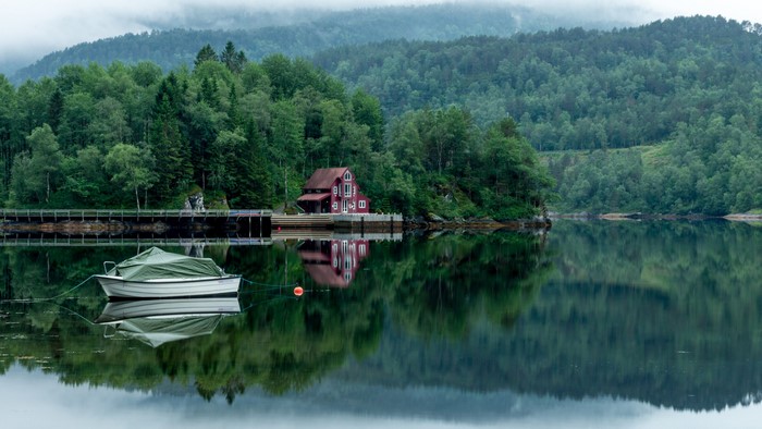 Red house on a lake with a boat and forest