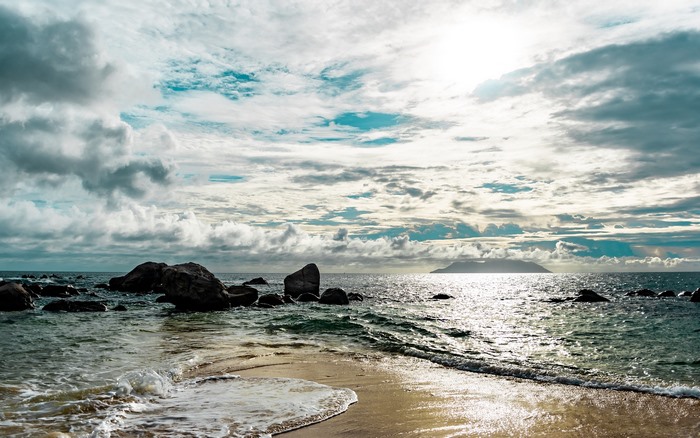 Ocean waves crash on a rocky beach with a distant island