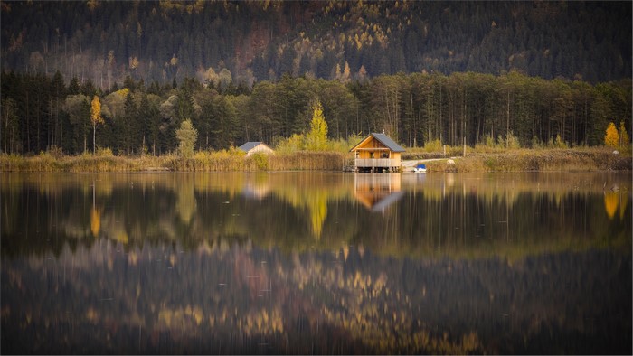 Wooden hut on a lake with forest reflection