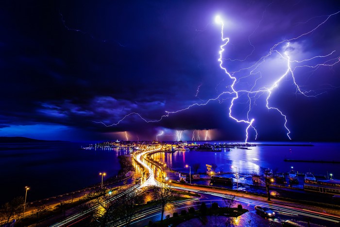 Cityscape with lightning strikes over water at night