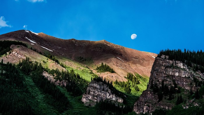 Mountains with moon and trees under blue sky