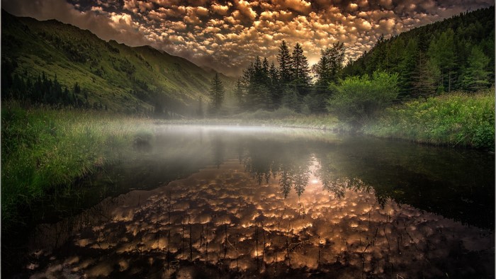 Misty lake reflecting dramatic clouds and mountains