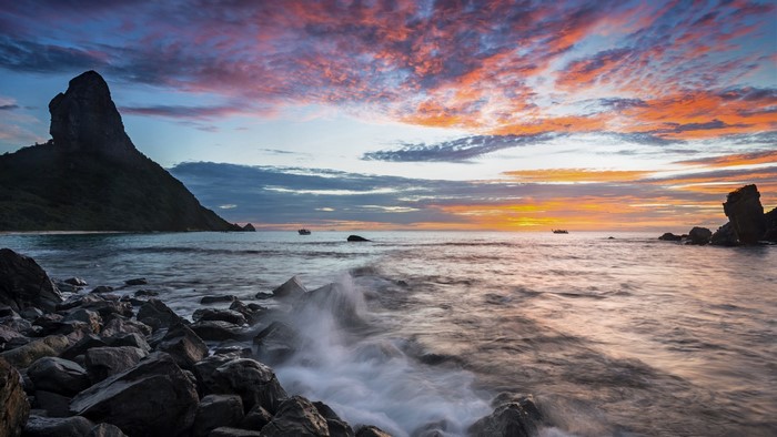 Sunset over the ocean with rocky shore and mountain