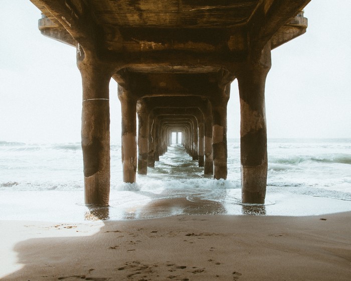 Under a pier on a sandy beach with waves
