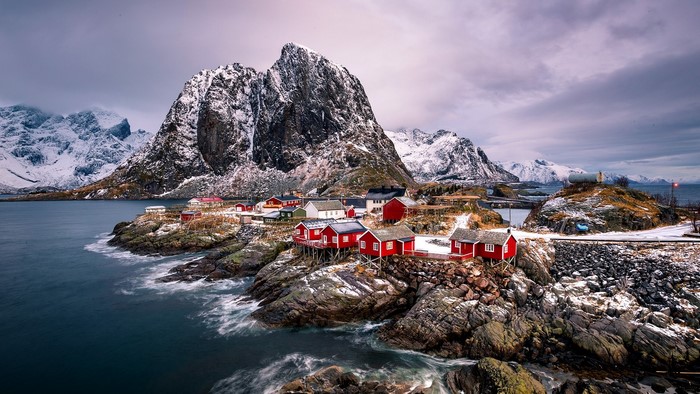 Red houses on rocky coast with snowy mountains in Lofoten Islands, Norway