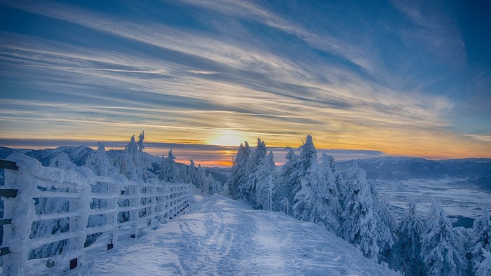Snowy mountain path at sunset with fence and trees