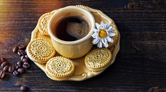 Coffee cup with cookies and coffee beans on a wooden surface