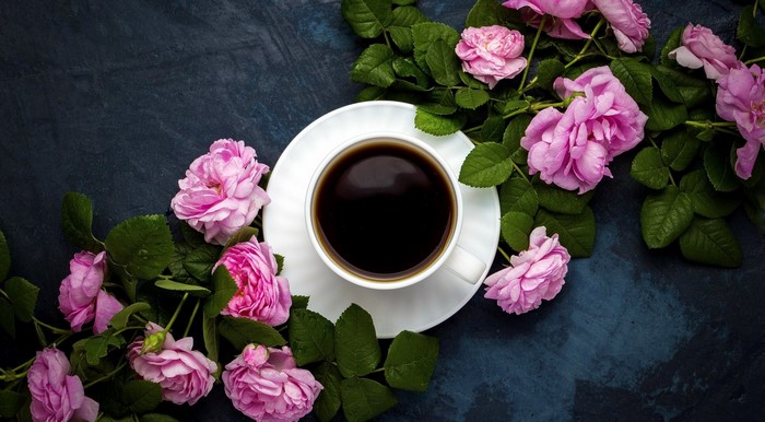 Cup of coffee with pink roses and green leaves