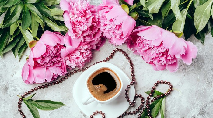 Pink peonies and coffee on a textured surface