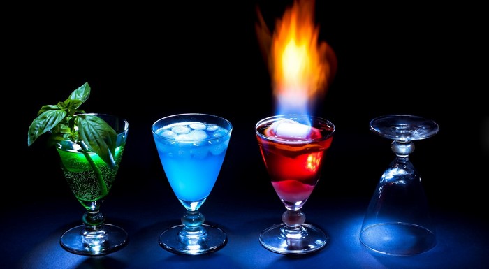 Four colorful cocktails with one on fire