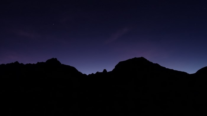 Dark mountains silhouette against a starry night sky