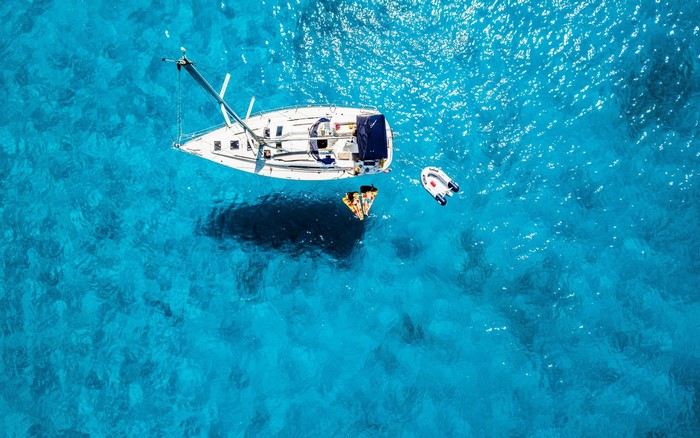 Sailboat and dinghy in clear blue ocean with people on float