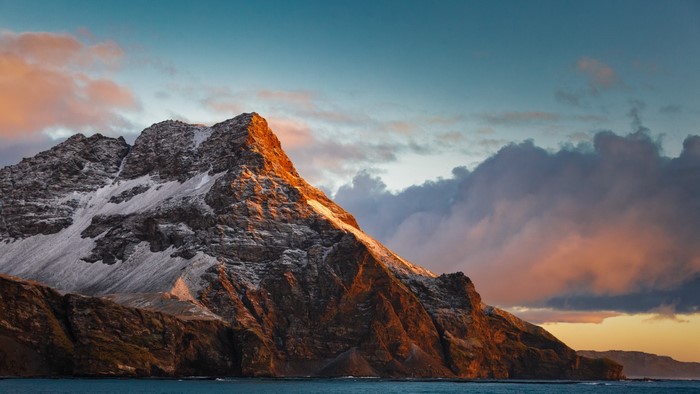 Snowy mountain range at sunset over the ocean