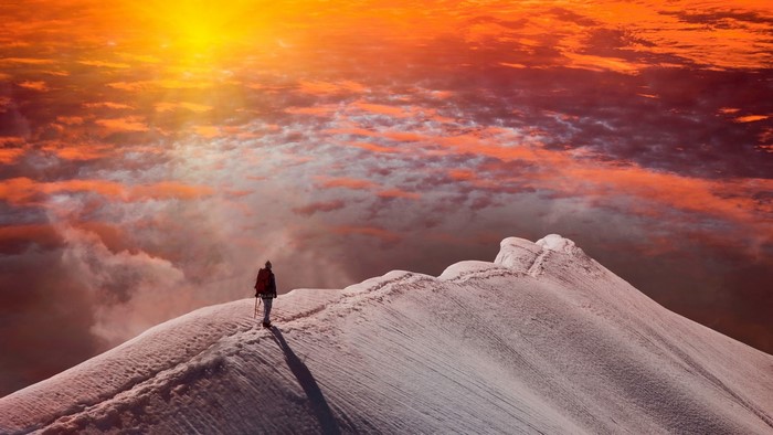 Hiker on snowy mountain ridge at sunset
