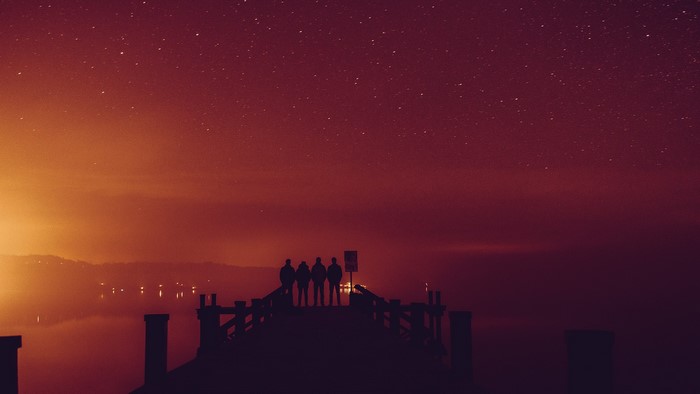 Four people on a pier under a starry sky