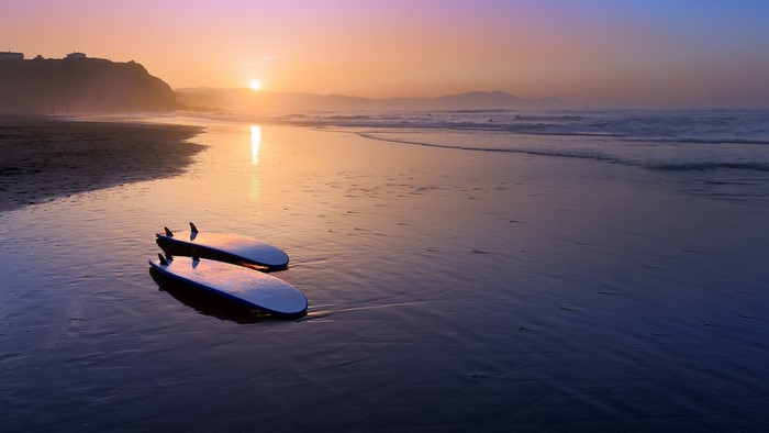 Surfboards on a beach at sunset with mountains