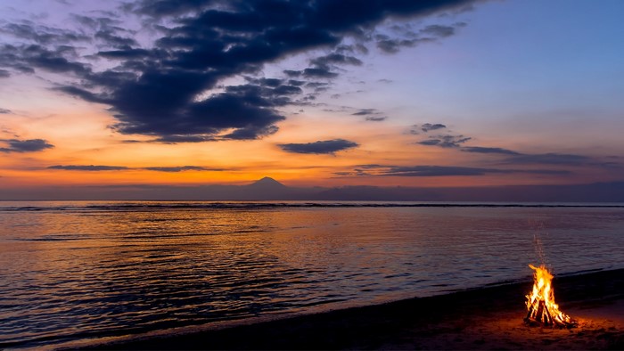 Bonfire on a beach at sunset with mountains in the distance