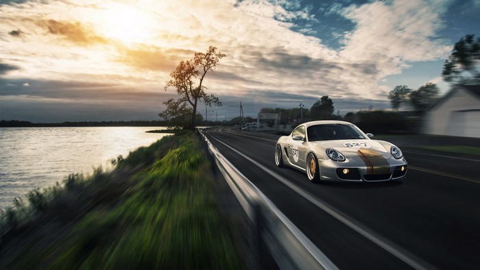 Silver Porsche 987 with racing stripes driving on a road