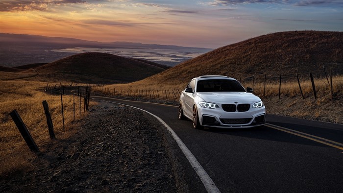 White BMW 2 Series driving on a winding road at sunset