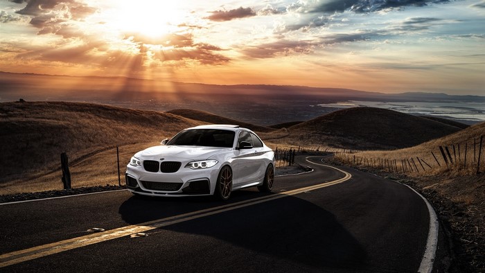 White BMW 2 Series on a winding road at sunset