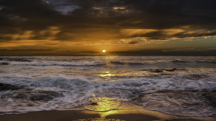 Sunset over the ocean with waves crashing on the shore