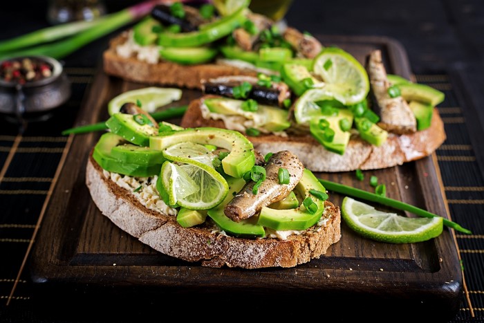 Avocado toast with sardines and lime on a cutting board