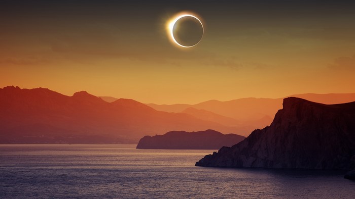 Solar eclipse over mountains and sea at sunset