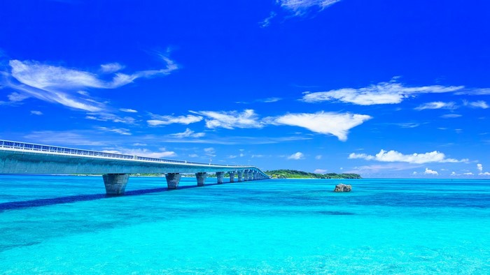 Bridge over turquoise water with island and clouds