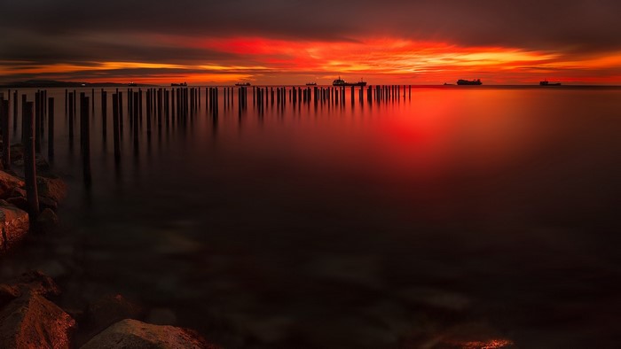 Sunset over the sea with ships and pier pilings