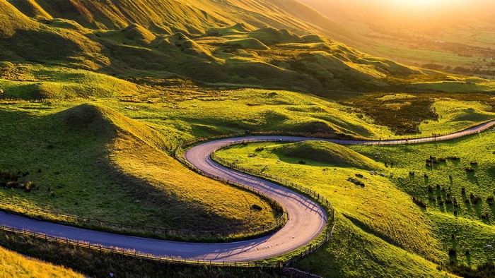 Winding road through green hills at sunrise in Edale Valley, UK