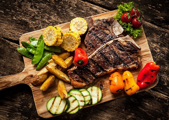 Grilled T-bone steak with grilled vegetables on a cutting board