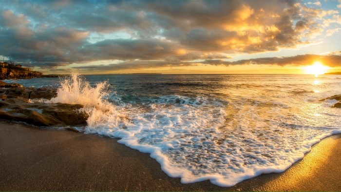 Sunset over the ocean with waves crashing on rocks and sand