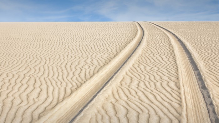 Tire tracks on sand dunes under a blue sky