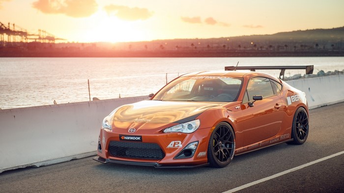 Orange sports car with a large spoiler parked by the water at sunset