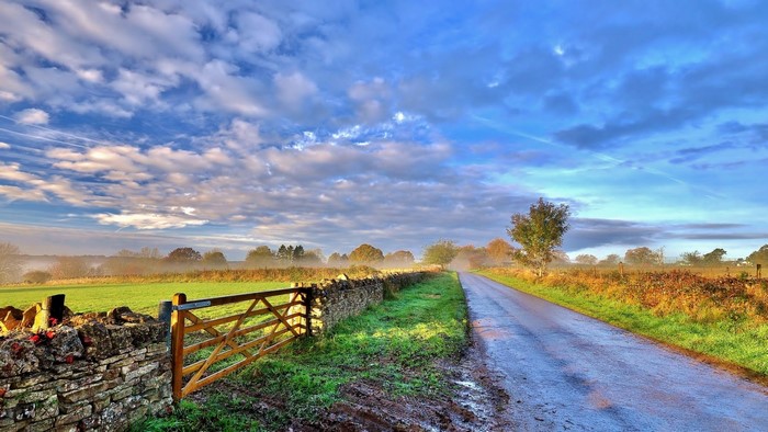 Country road with stone wall and wooden gate