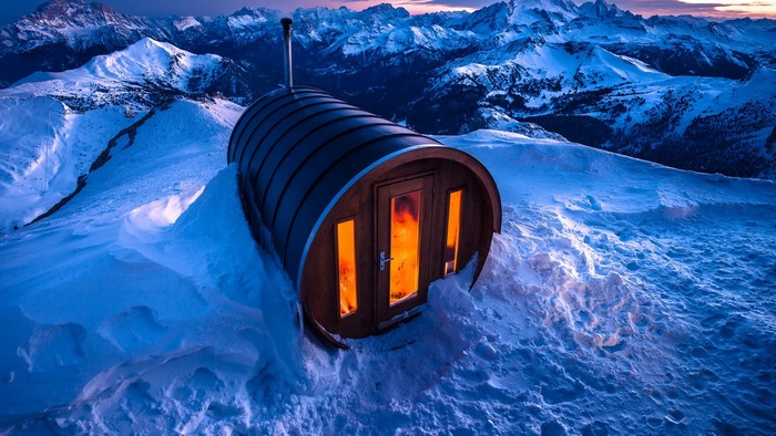 Barrel sauna in snowy Alps mountains at dusk
