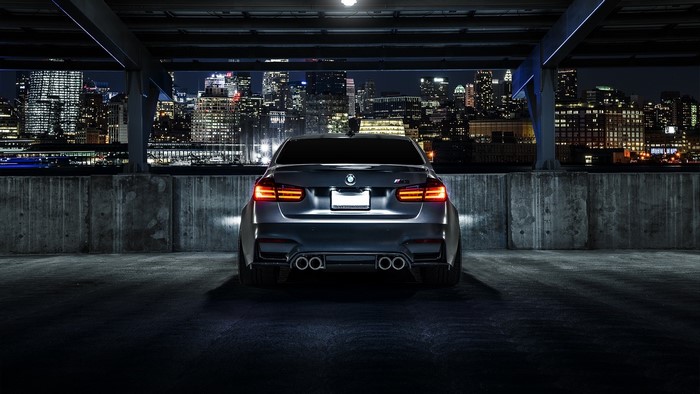 BMW M3 Sedan in a parking garage at night with city skyline