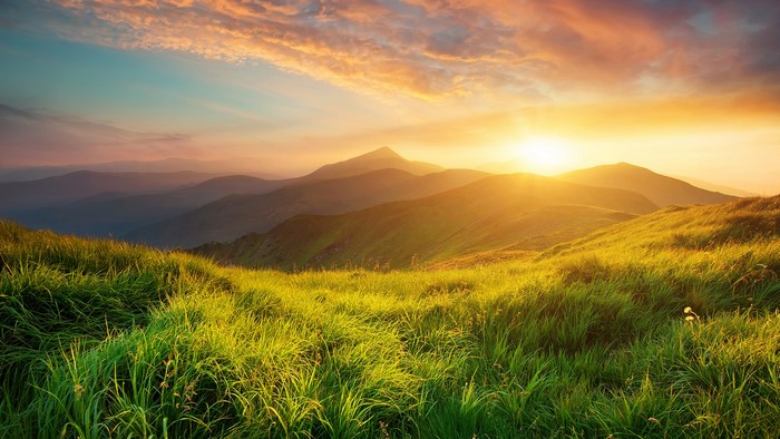Sunrise over mountains with green grass and clouds
