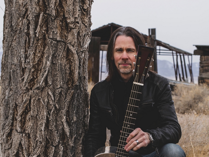 Myles Kennedy with guitar in front of abandoned building
