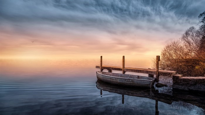 Boat docked at a pier on a calm lake at sunset