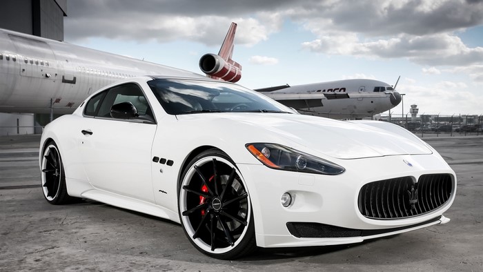 White Maserati GranTurismo parked by an airplane
