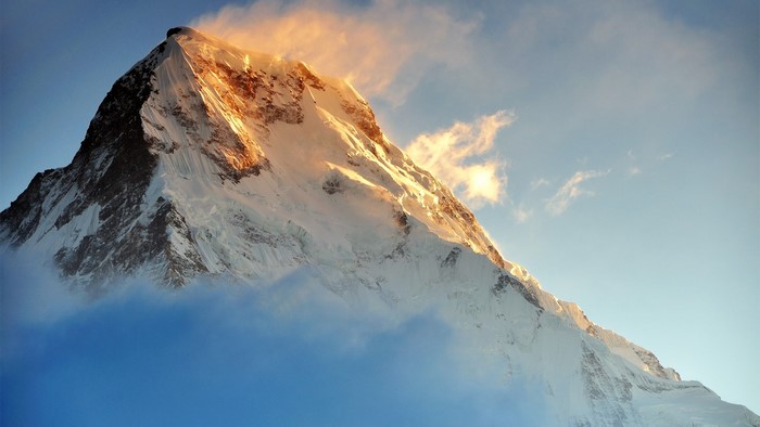 Snowy mountain peak at sunrise with clouds